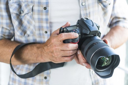fotografo maschio che tiene la macchina fotografica della foto del dslr in mani